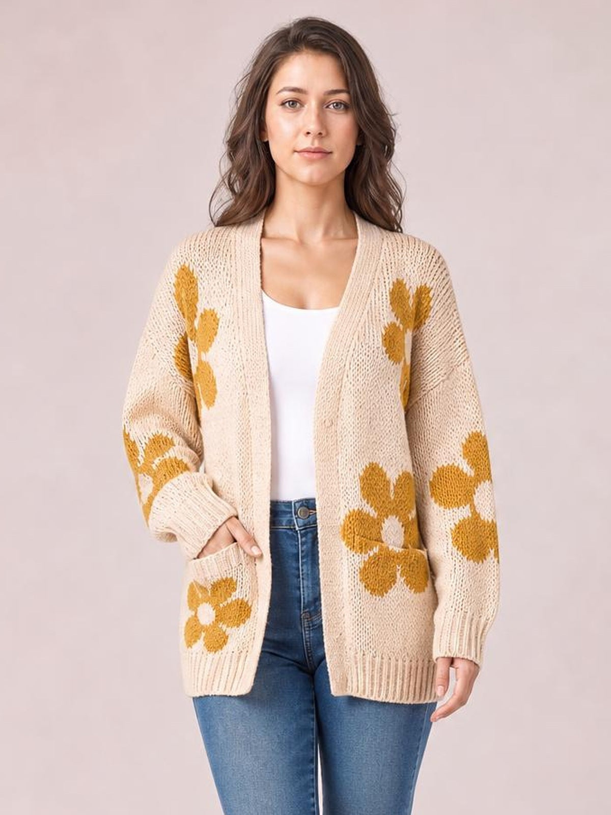 Model wearing a beige open-front long-sleeve cardigan with mustard flower motifs, relaxed silhouette, ribbed cuffs and hem, and front patch pockets.