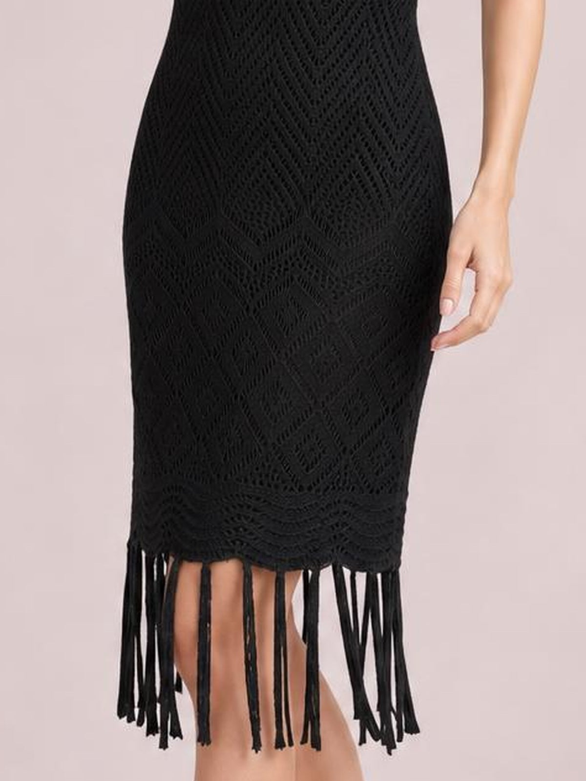 Close-up of a model wearing a black sleeveless openwork cover-up dress with a fitted silhouette, geometric texture, and long fringe trim at the hem.