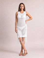 Model poses with one hand on her hip in a white sleeveless openwork cover-up dress with a fitted silhouette and long tassel fringe hem.