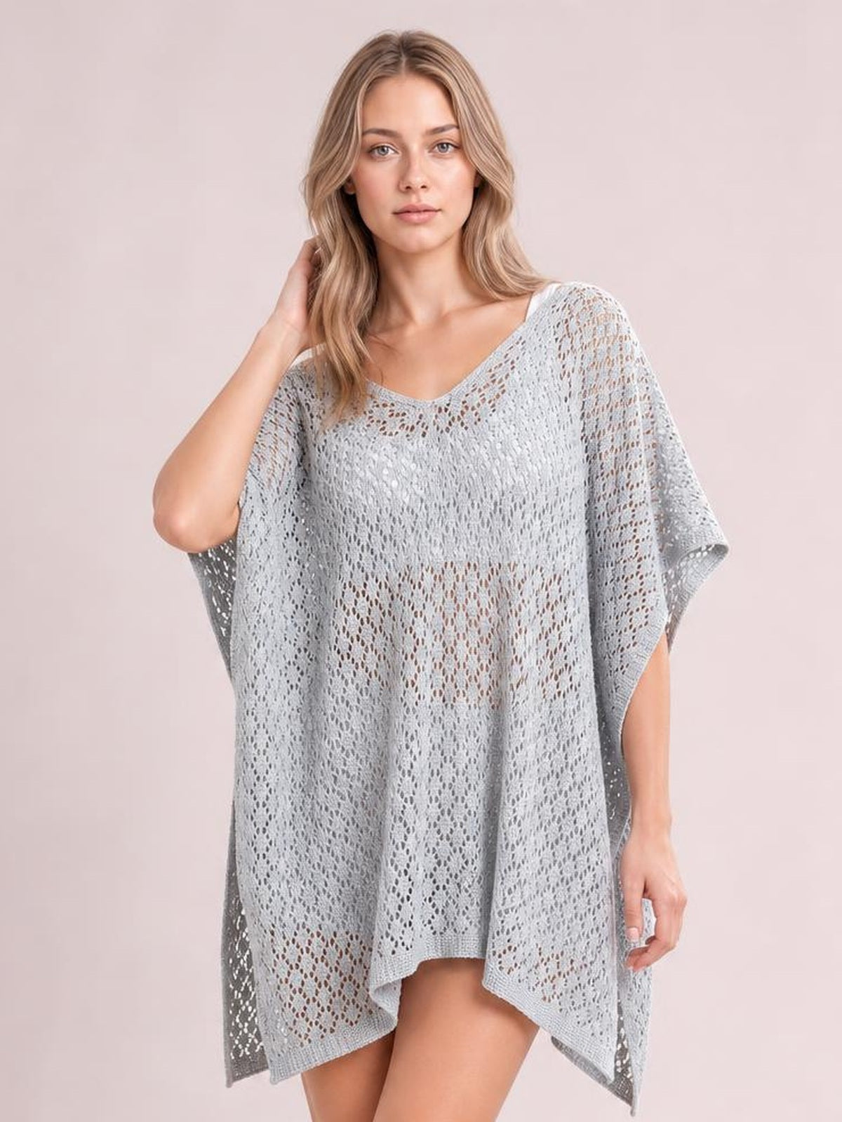 Model poses in a light gray semi-sheer openwork cover up with a scoop neck, loose poncho silhouette, short sleeves, and asymmetrical hem.