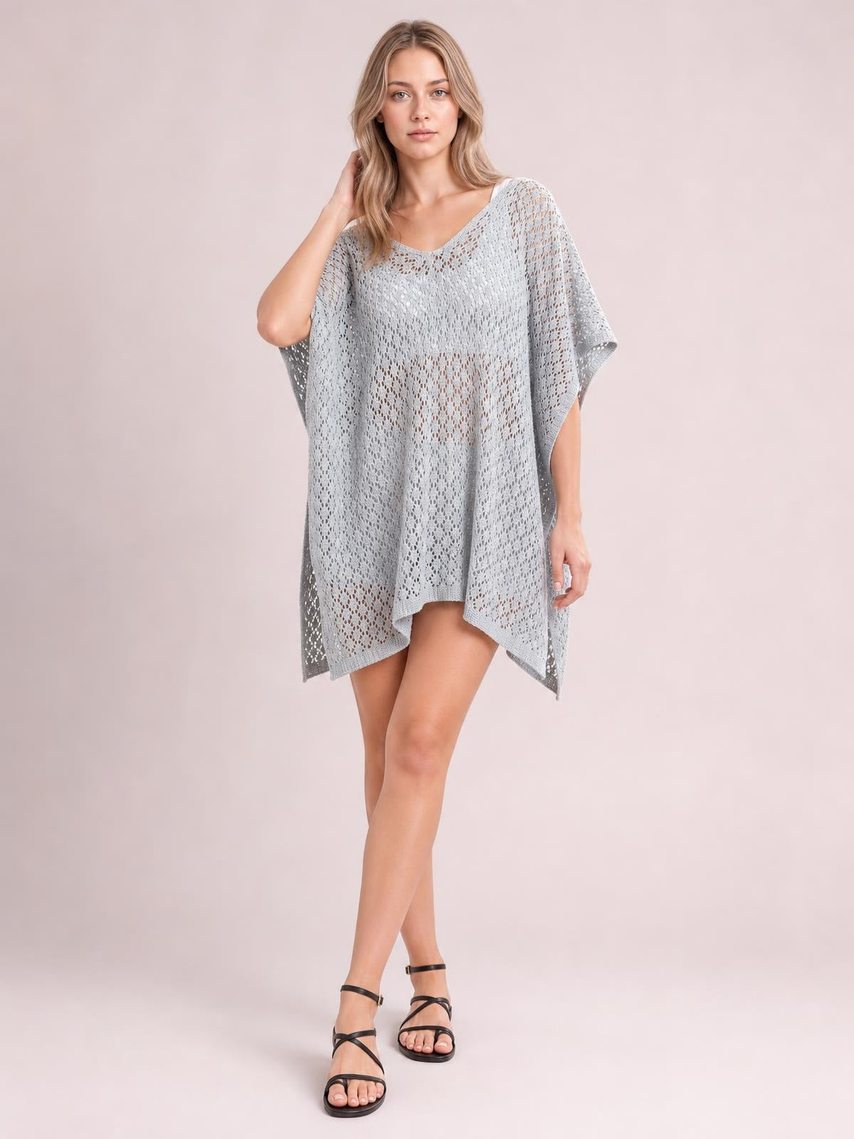 Model wearing a light gray semi-sheer openwork cover-up with a scoop neck, relaxed poncho silhouette, side slits, short sleeves, and an asymmetrical hem.