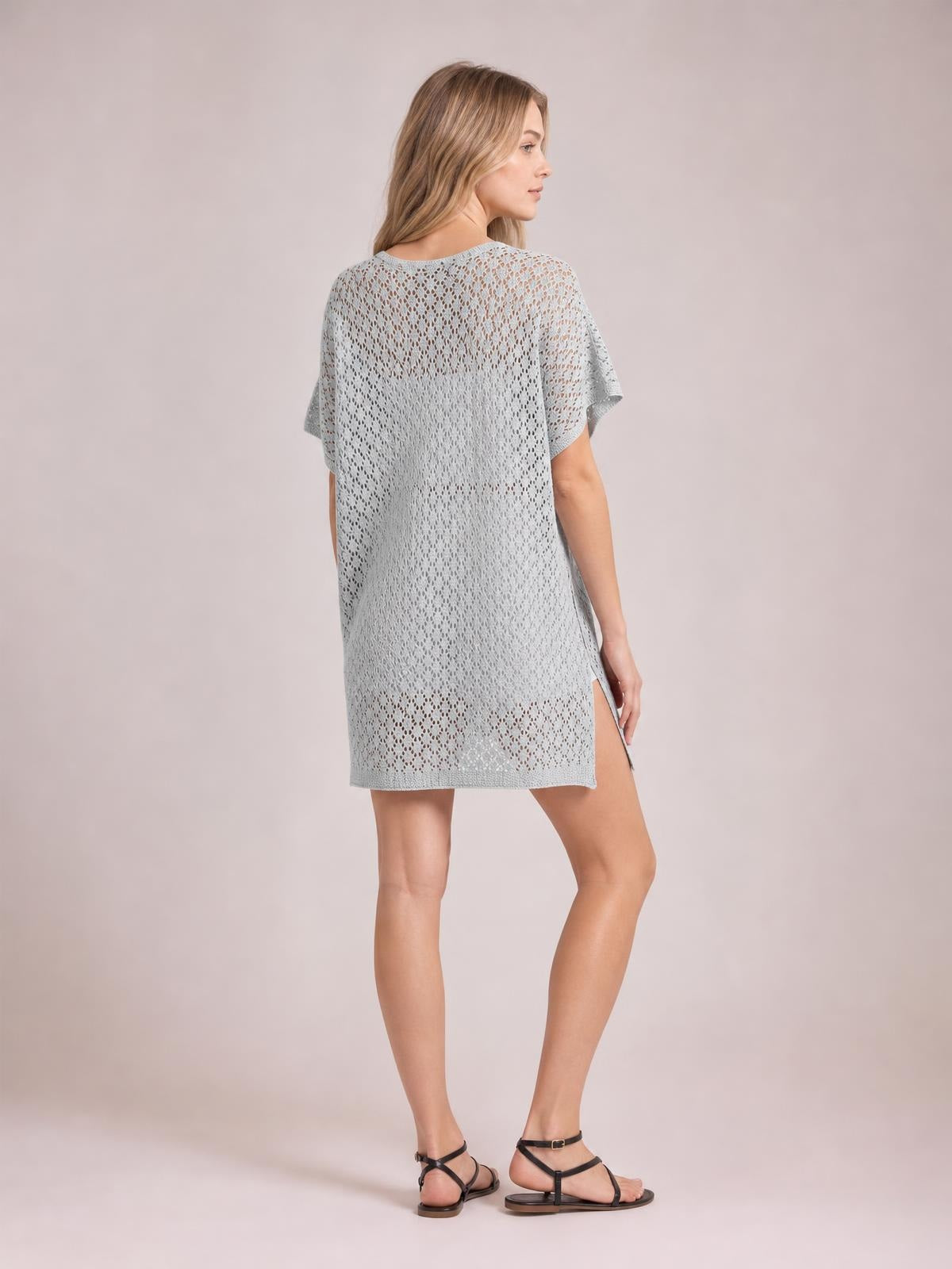 Model in a side pose wears a light gray semi-sheer openwork cover up with a scoop neck, loose silhouette, short sleeves, and side slit.