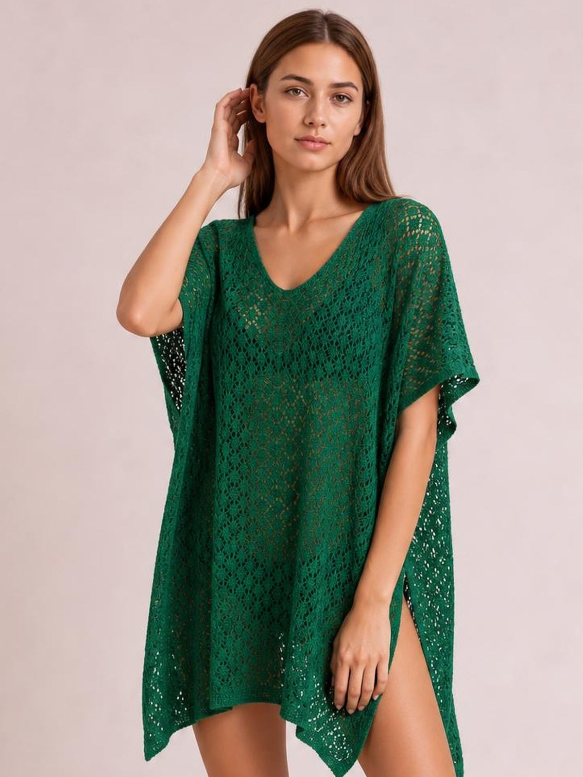 Model wearing a deep green semi-sheer openwork cover up with a scoop neck, loose draped silhouette, short sleeves, and side slit, posing with one hand by her hair.