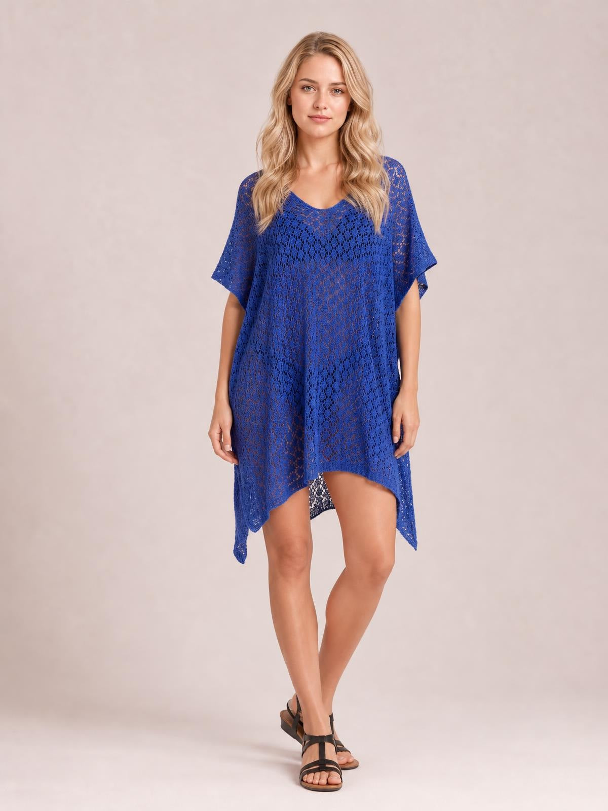 Model poses with crossed legs in a royal blue semi-sheer openwork cover up featuring a scoop neckline, short sleeves, and an asymmetric slit hem.