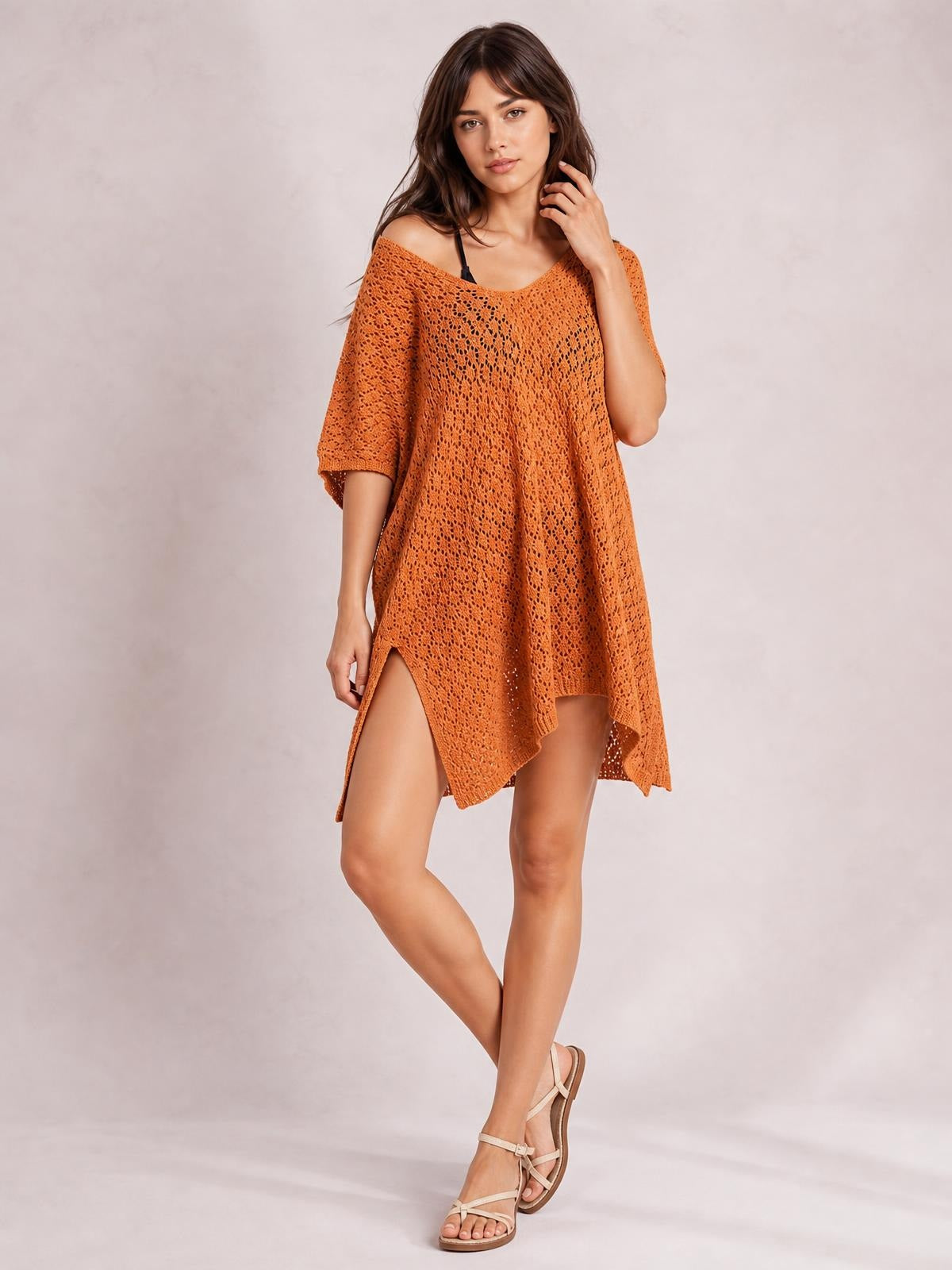 Model poses in an orange openwork cover up with a scoop neck, semi-sheer knit texture, relaxed oversized silhouette, and asymmetrical slit hem.