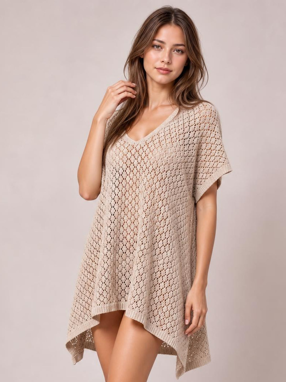 A model poses in a beige semi-sheer openwork cover up with a scoop neckline, short sleeves, relaxed silhouette, and asymmetrical slit hem.