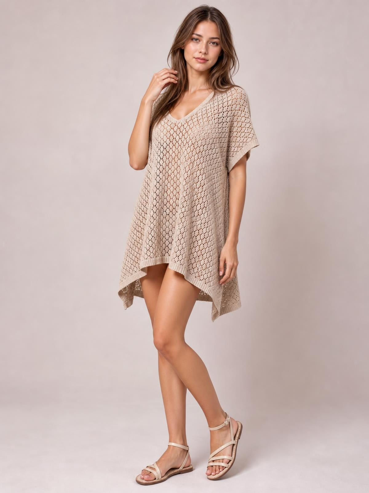 A model poses in a beige semi-sheer openwork cover-up with a scoop neck, short sleeves, relaxed silhouette, and asymmetrical slit hem.