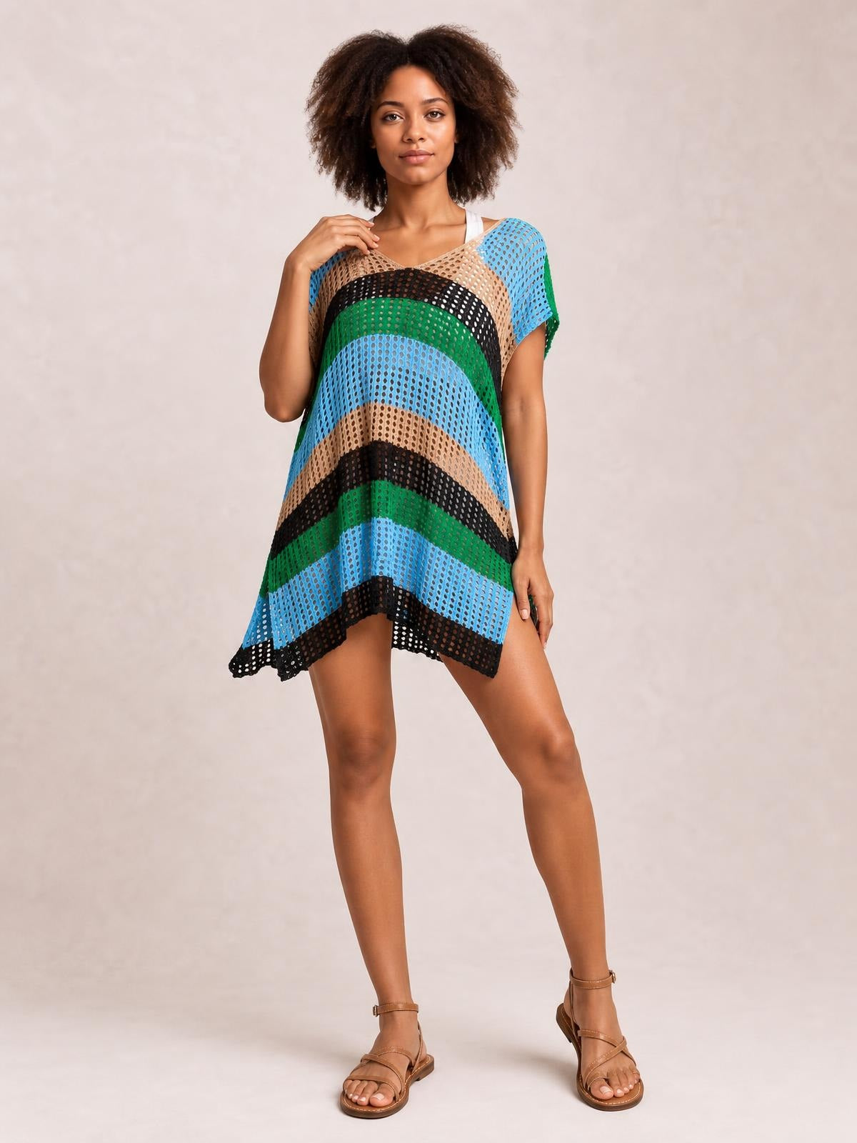 Model poses in a colorful striped V-neck short sleeve cover up with a semi-sheer openwork knit, relaxed tunic silhouette, and asymmetrical hem.