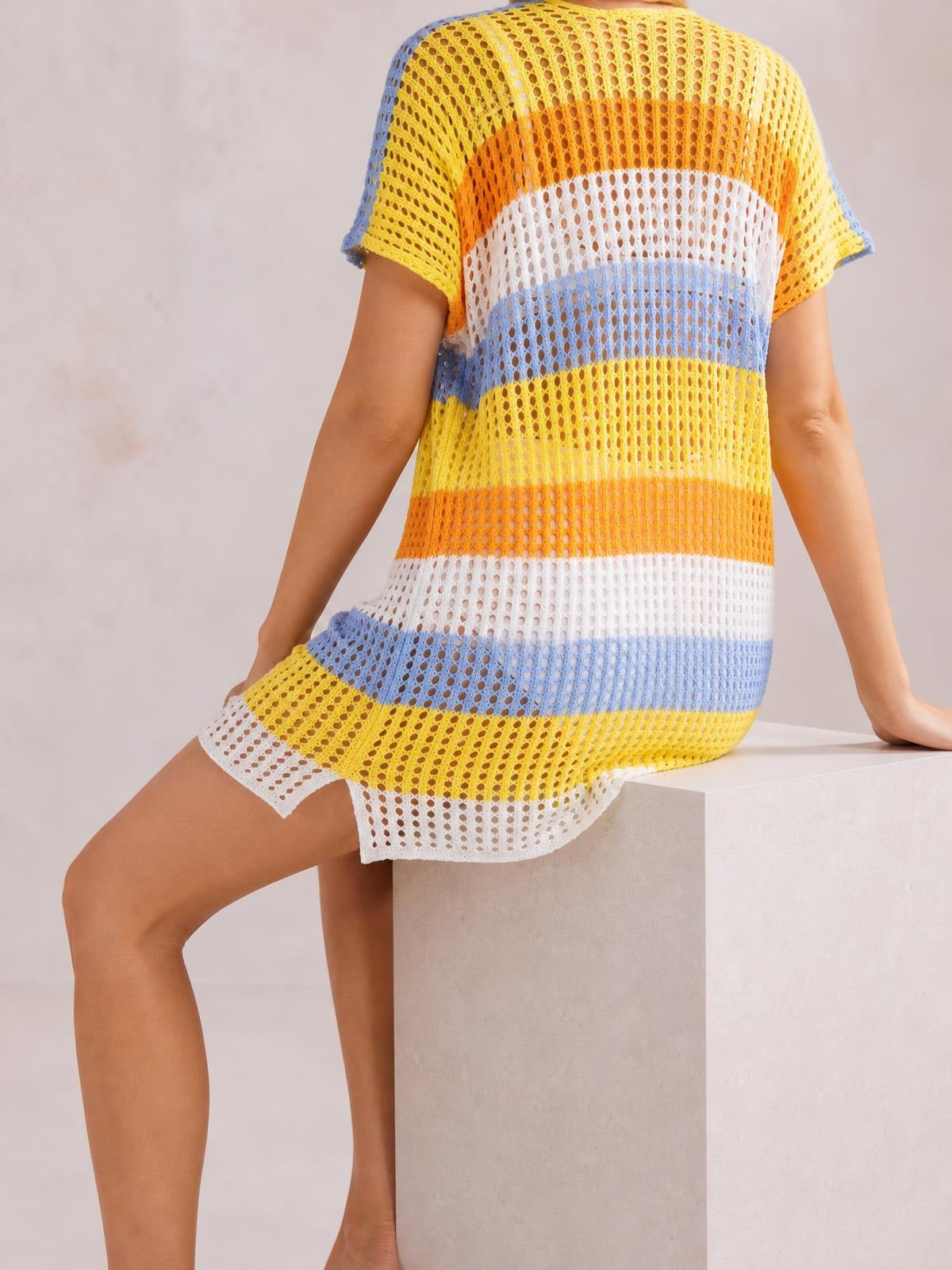 Model seated with one hand resting behind her, wearing a relaxed short-sleeve cover-up in colorful horizontal stripes with stretchy, semi-sheer openwork.