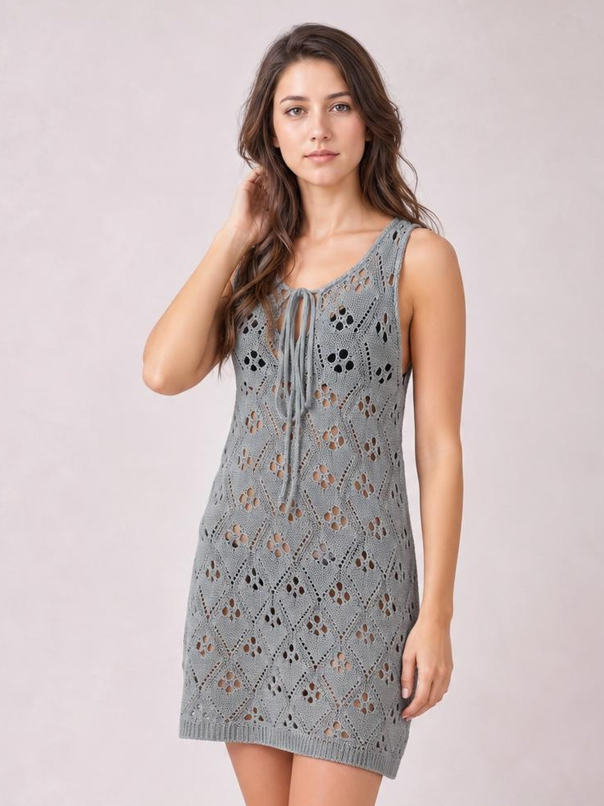 Model poses in a gray semi-sheer openwork cover-up with a sleeveless straight mini silhouette, stretchy knit construction, and a front tie neck.