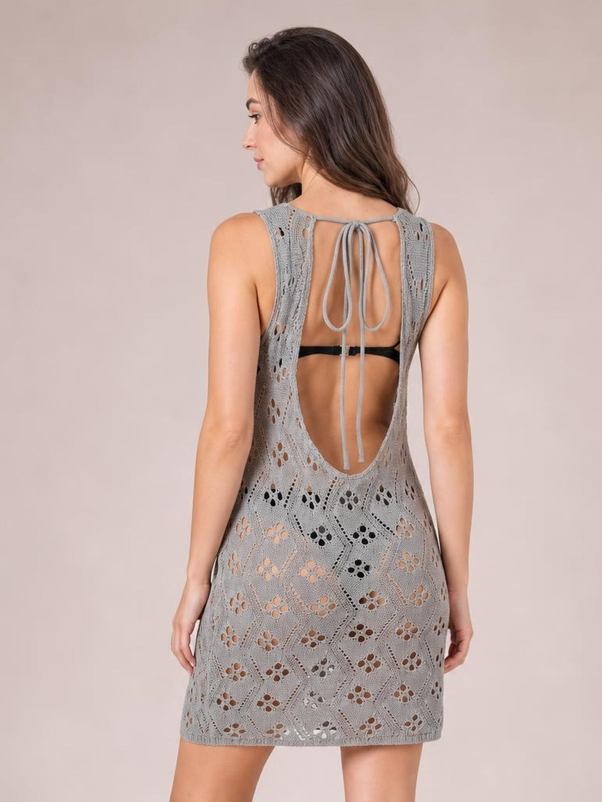 A model poses from the back in a gray semi-sheer openwork cover-up with a tie neck, sleeveless cut, open back, and relaxed mini silhouette.