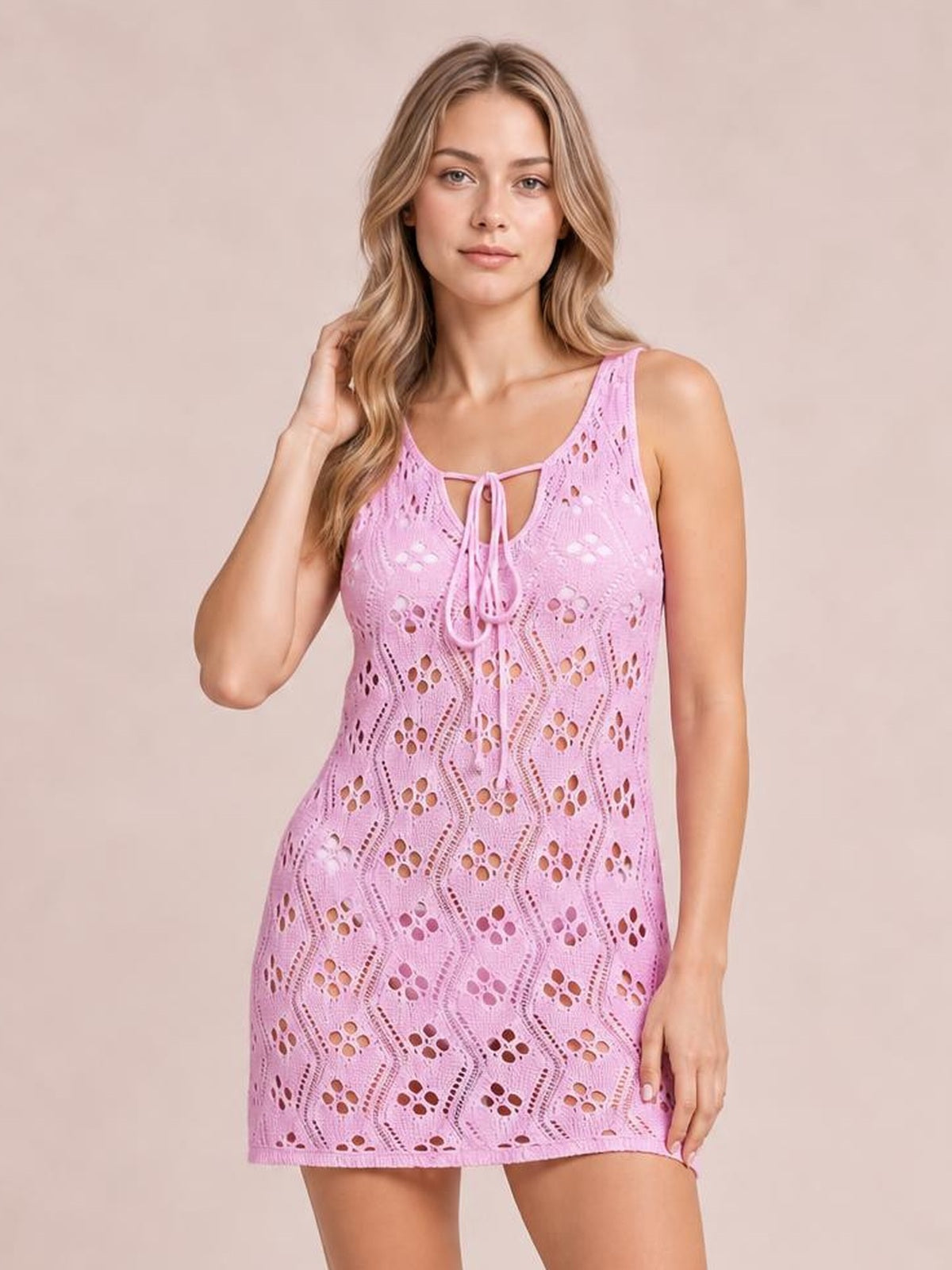 A model poses in a pink sleeveless Openwork Tie Neck Cover-Up with a semi-sheer patterned knit, front tie detail, and fitted short silhouette.