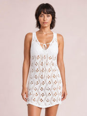 Model stands facing forward in a white semi-sheer openwork cover-up with sleeveless straps, a tie neckline, stretchy construction, and a straight mini-length silhouette.