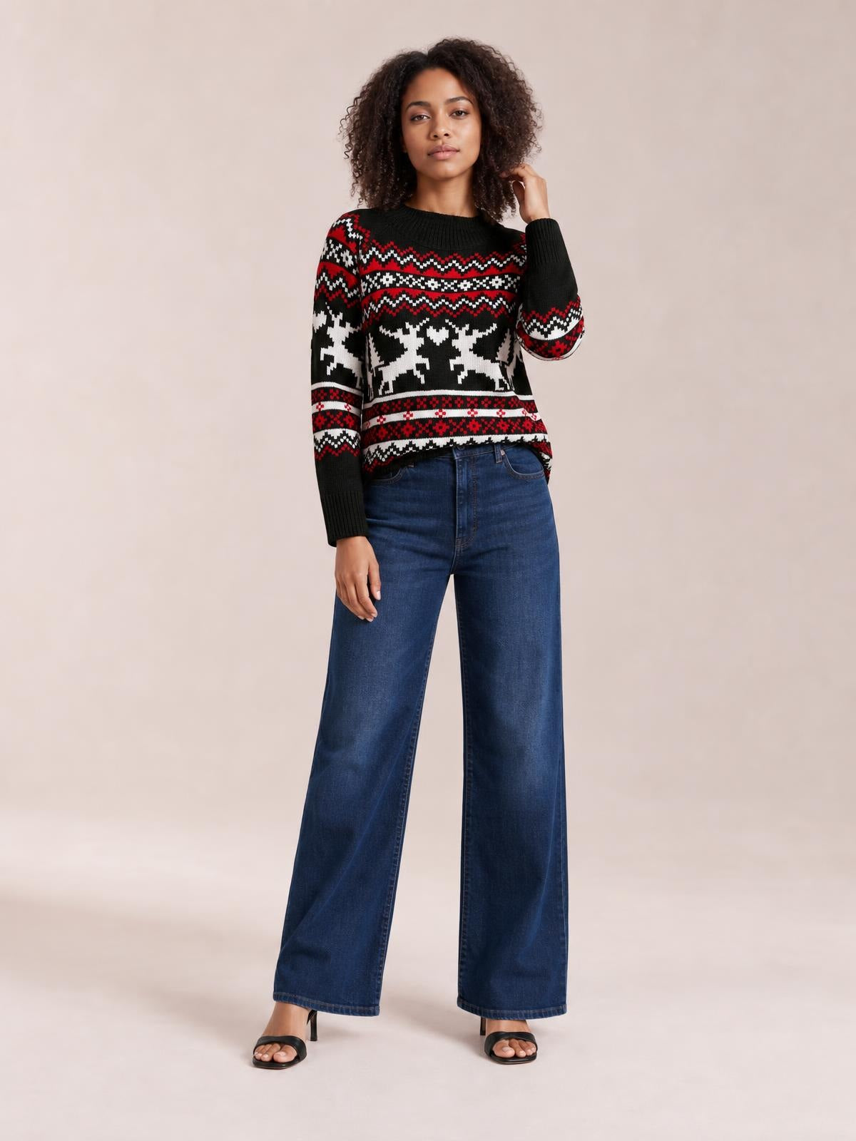 Model wears a black reindeer round-neck long-sleeve sweater with red and white Fair Isle patterns, ribbed cuffs and hem, and a relaxed silhouette.