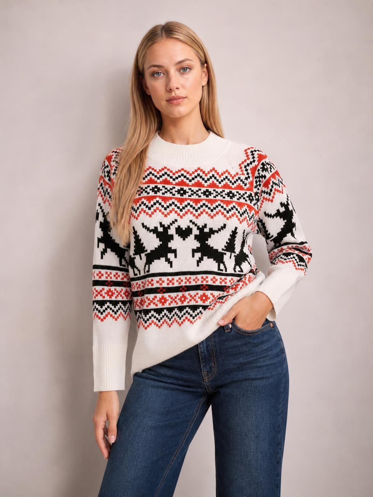 Model poses with one hand at her jeans pocket, wearing a white reindeer round neck long sleeve sweater with red and black Fair Isle-style knit patterns and ribbed cuffs.