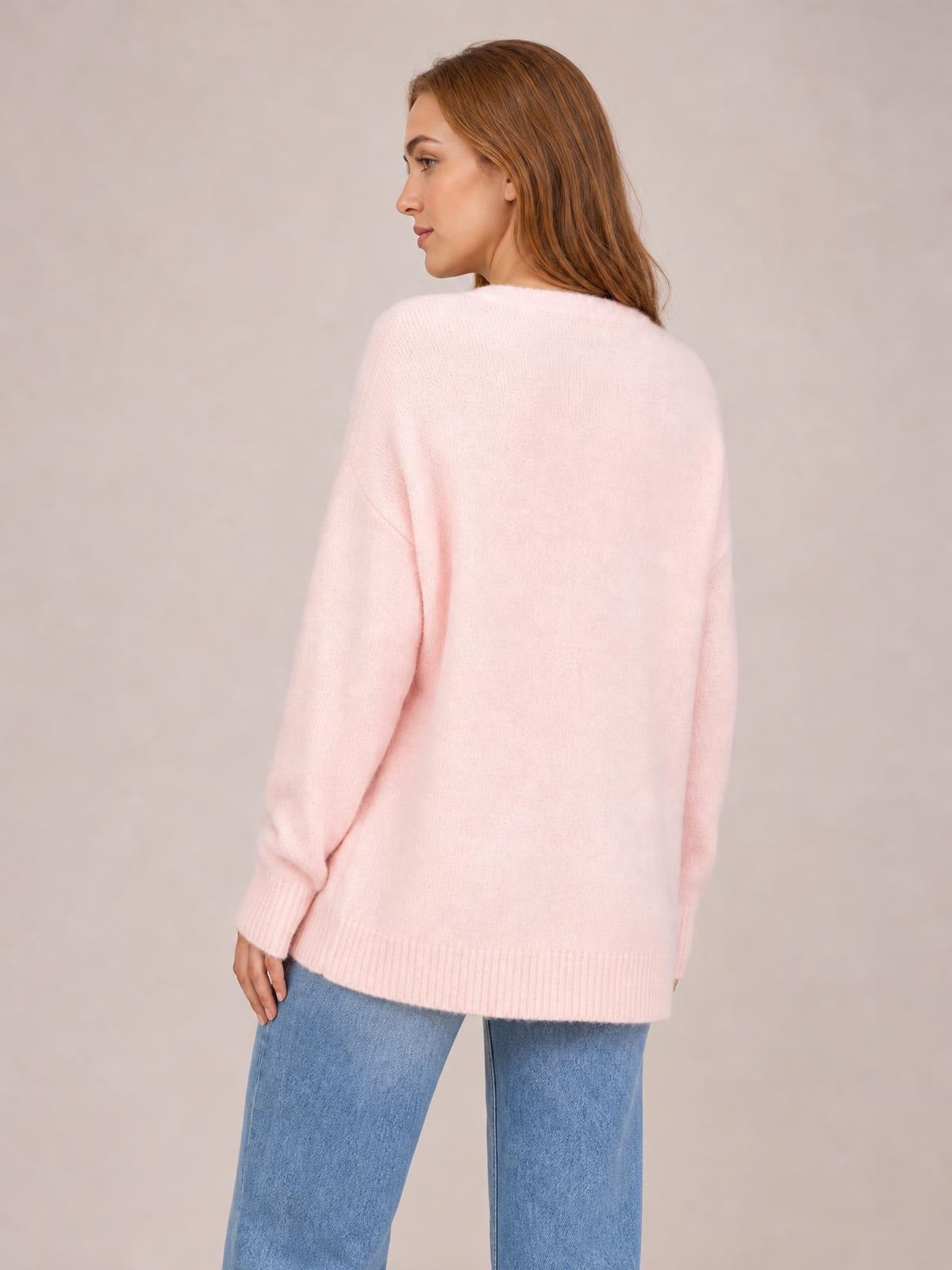 A model looks over her shoulder wearing a soft pink round neck ribbed sweater with long sleeves, a relaxed regular-length silhouette, and ribbed cuffs and hem.