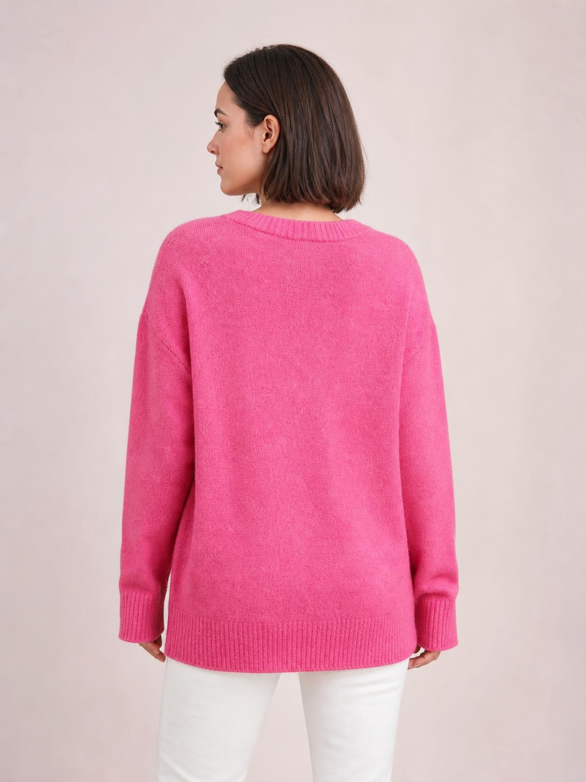 Model in a back-facing pose wears a bright pink solid ribbed sweater with a round neck, long sleeves, ribbed cuffs and hem, and a relaxed regular-length silhouette.