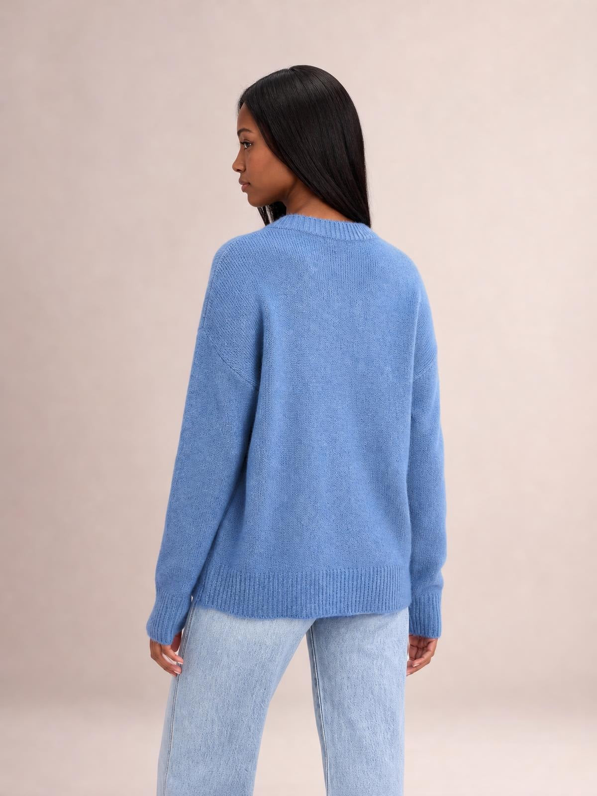 Model turned slightly sideways wears a solid blue ribbed sweater with a round neck, long sleeves, regular length, and relaxed silhouette.