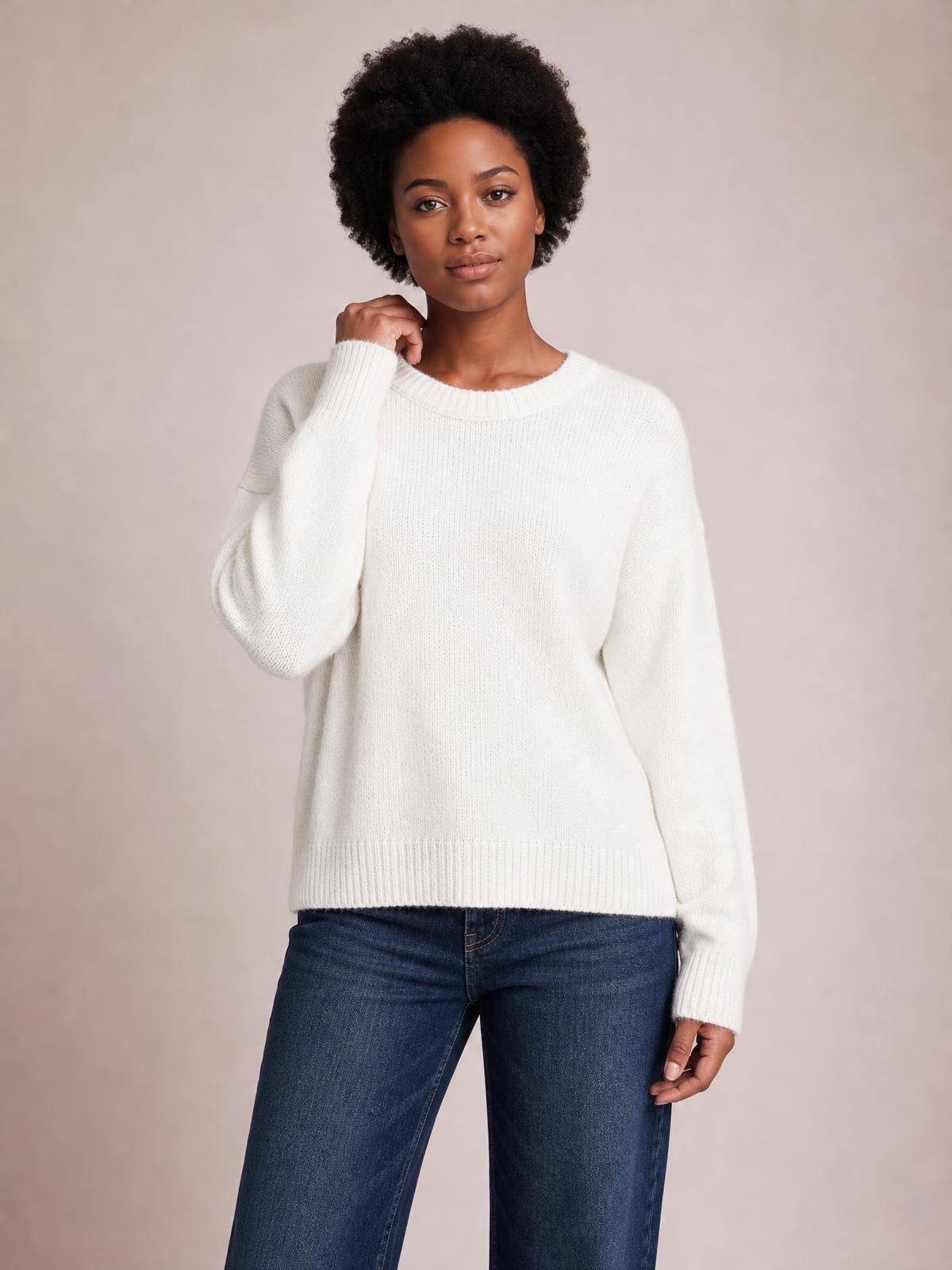 A model poses in a white solid ribbed sweater with a round neck, long regular sleeves, a relaxed regular-length silhouette, and ribbed cuffs and hem.