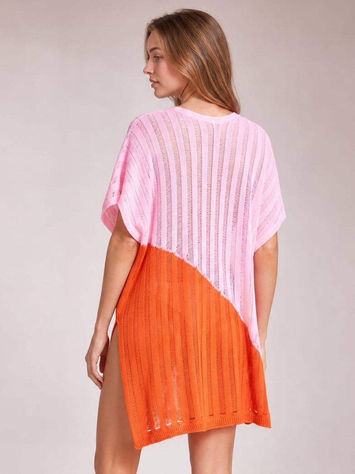 Model shown from behind in a loose sheer pink and orange color-block cover-up with vertical openwork texture, short sleeves, and a high side slit.