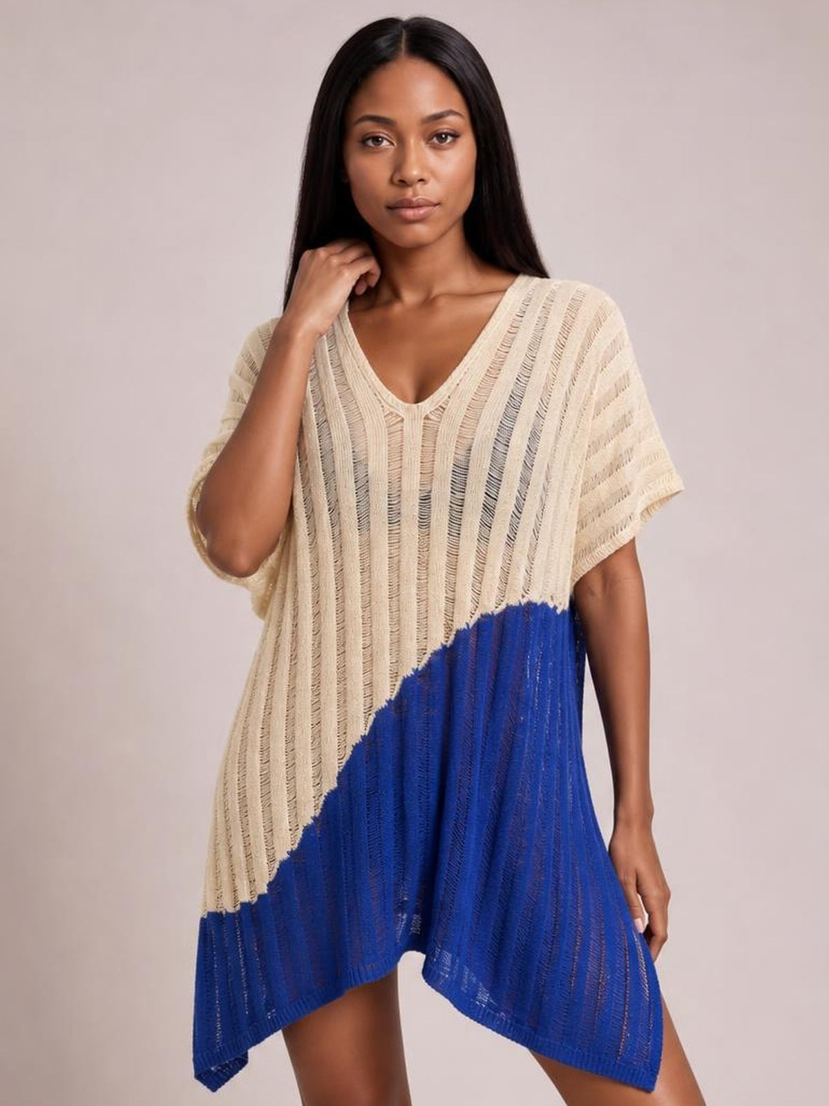 A model poses in a sheer cream and cobalt blue color-block cover-up with a V-neck, short sleeves, textured knit, slit hem, and asymmetrical silhouette.