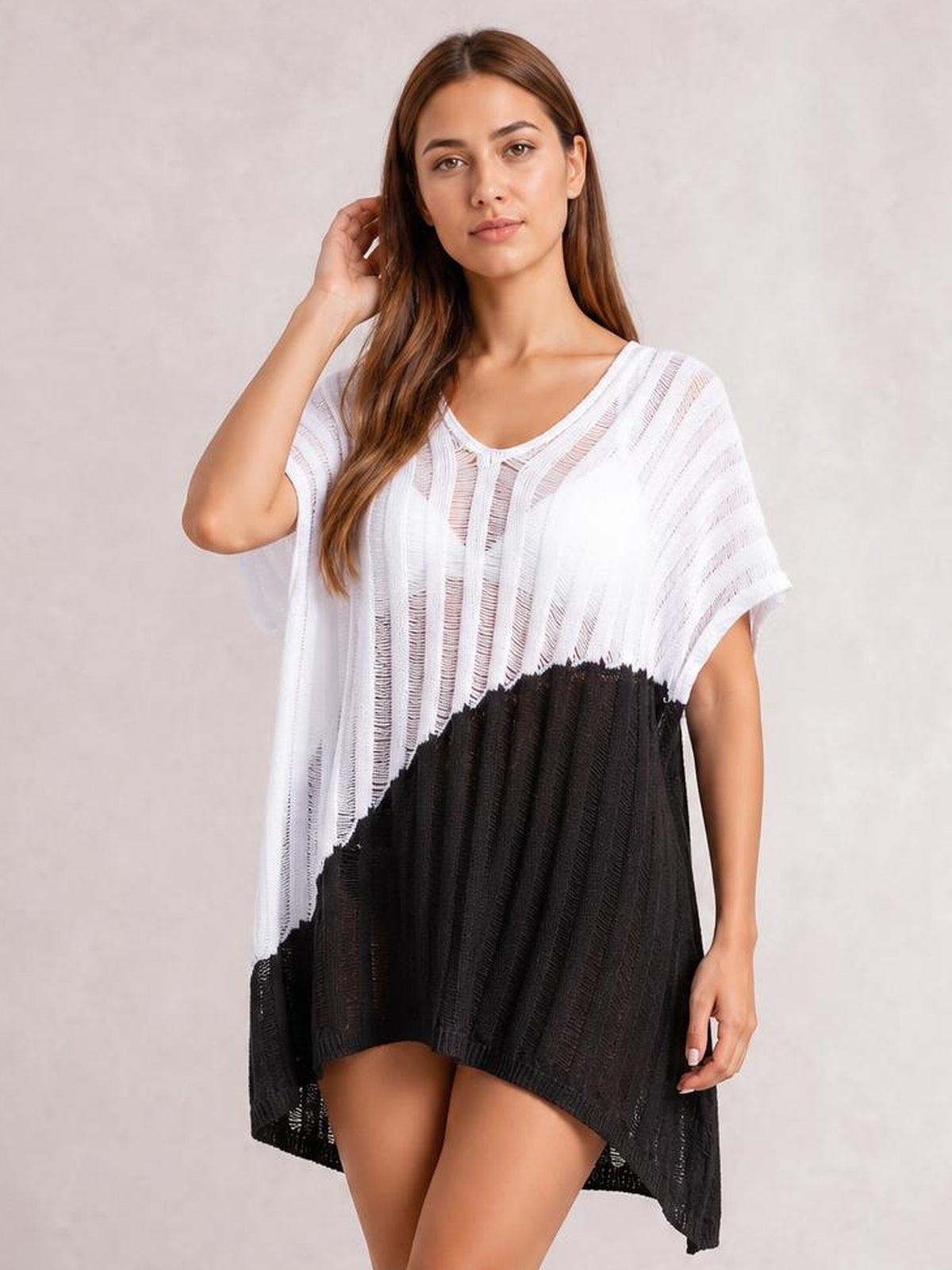 A model poses with one hand by her hair in a sheer white-and-black color-block cover up featuring a loose draped silhouette, short sleeves, and a high-low hem.