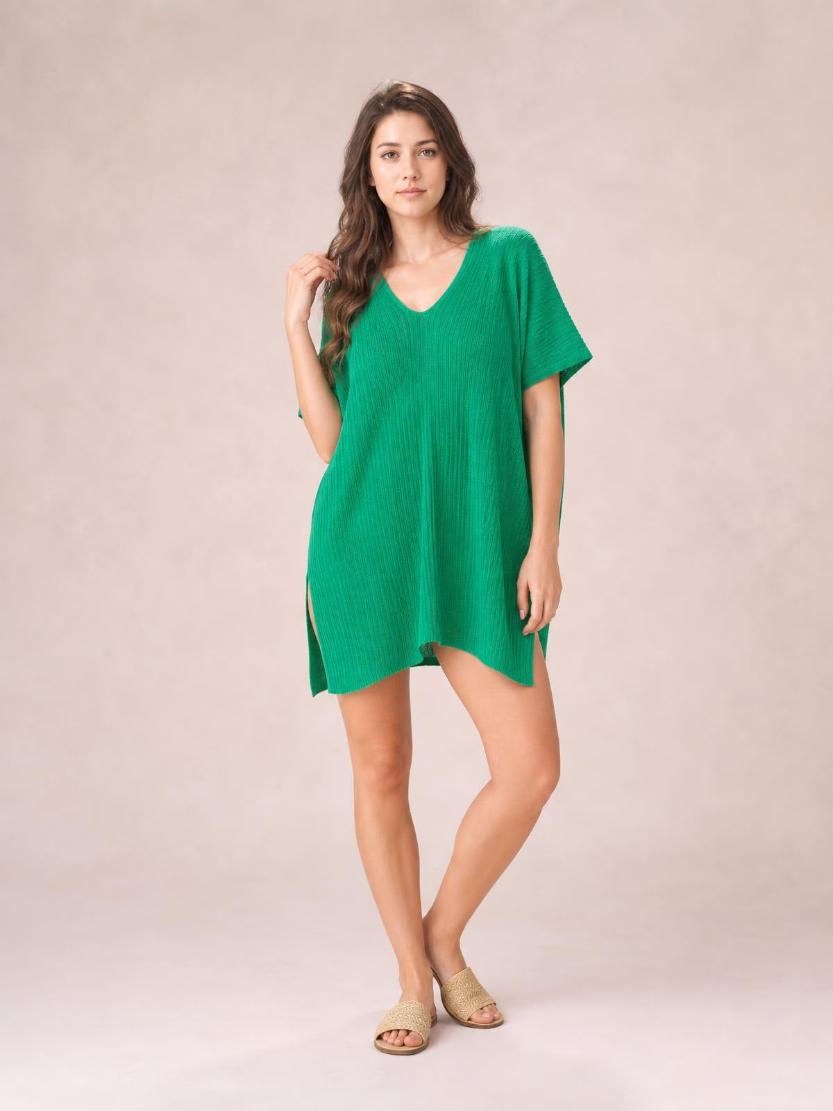 Model poses in a bright green semi-sheer cover up with a slit V-neck, short sleeves, relaxed silhouette, and asymmetrical hem.