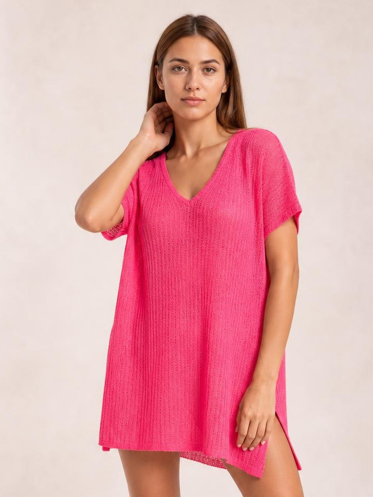 Model poses in a bright pink semi-sheer cover up with a slit V-neck, short sleeves, textured knit construction, and a relaxed oversized silhouette.