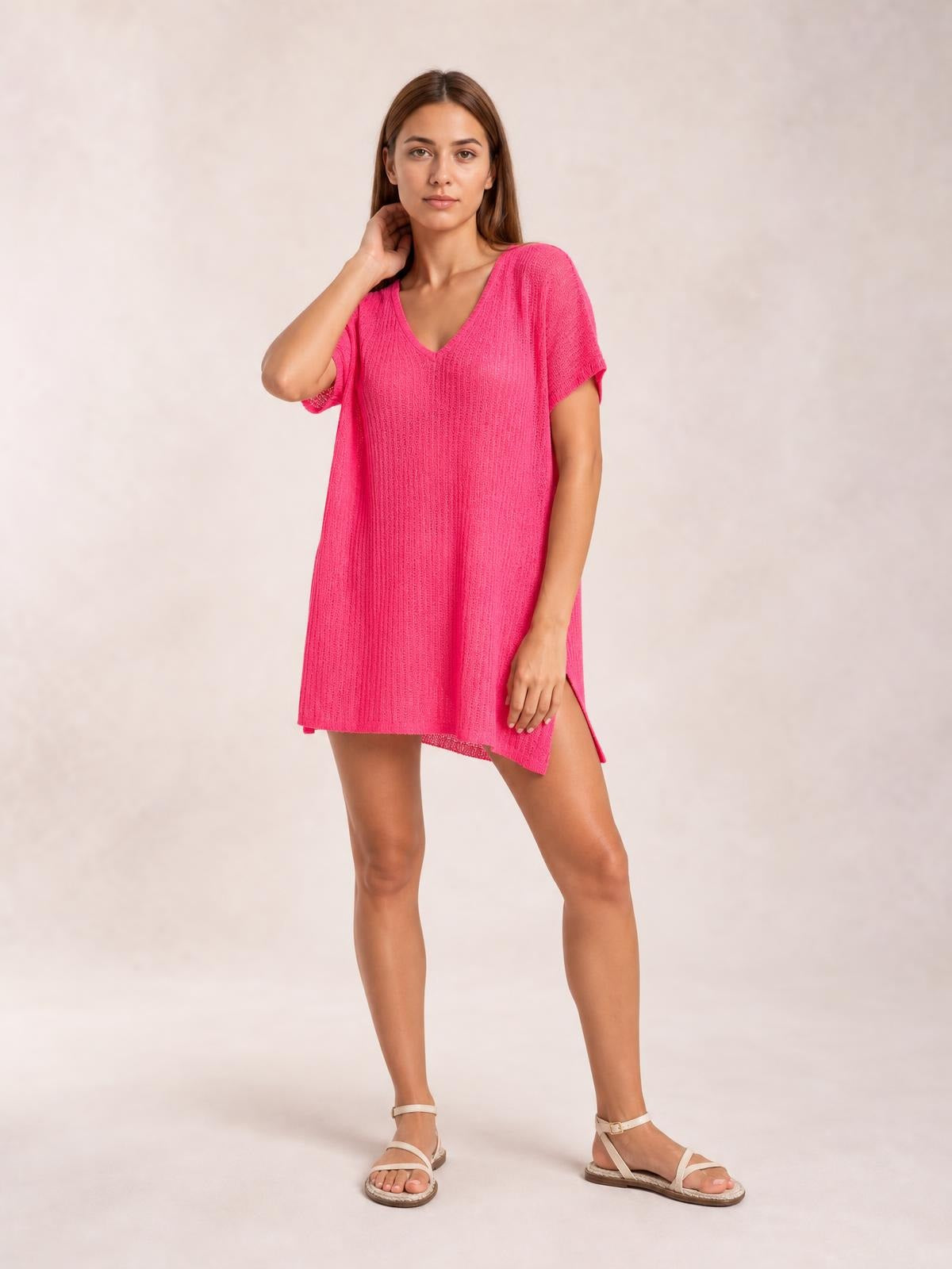 A model poses in a bright pink semi-sheer cover-up with a V-neck, short sleeves, relaxed tunic silhouette, textured knit, and visible side slit.