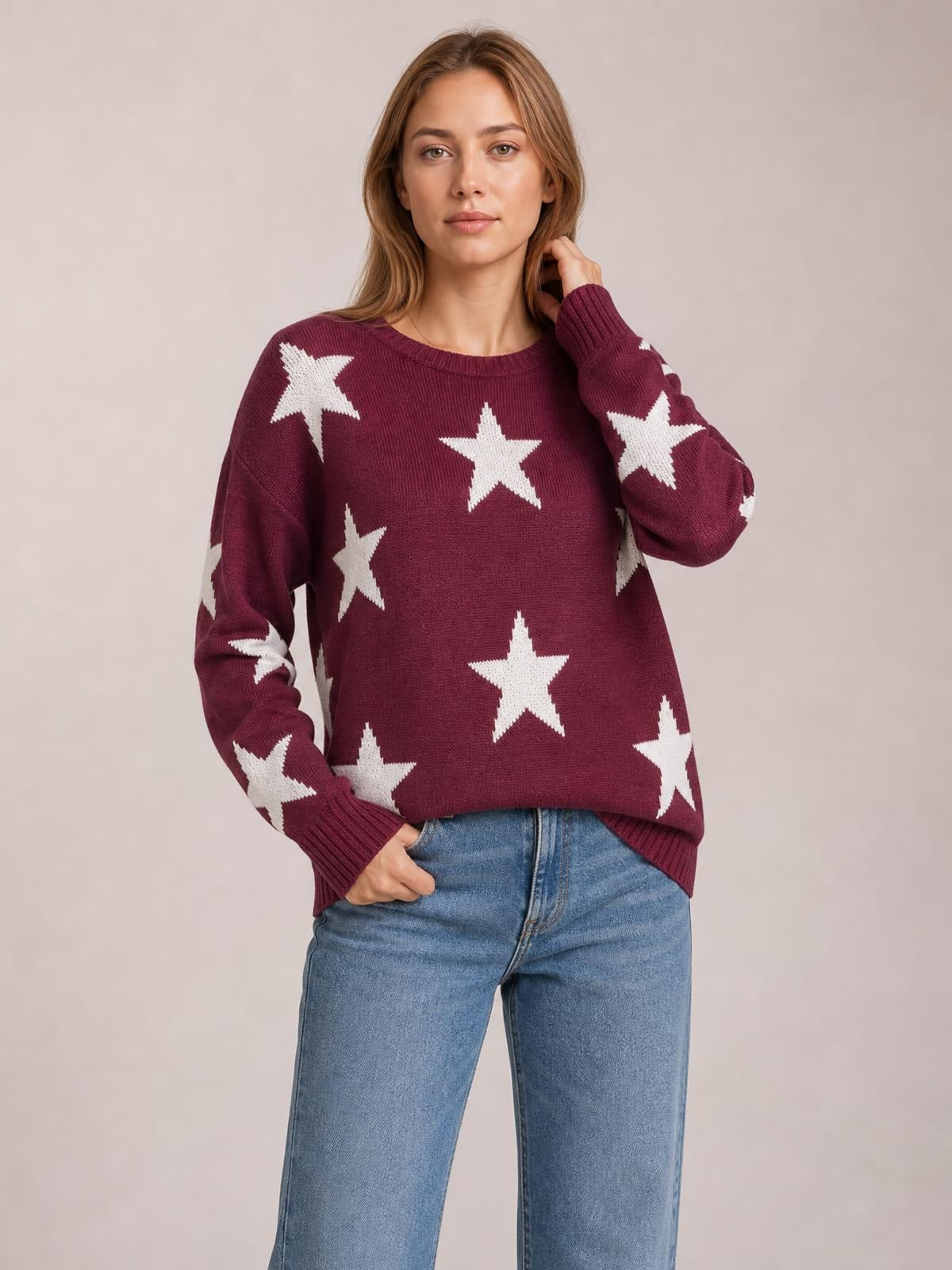 Model poses in a burgundy round neck dropped shoulder sweater with white star pattern, ribbed trim, relaxed silhouette, and long sleeves.