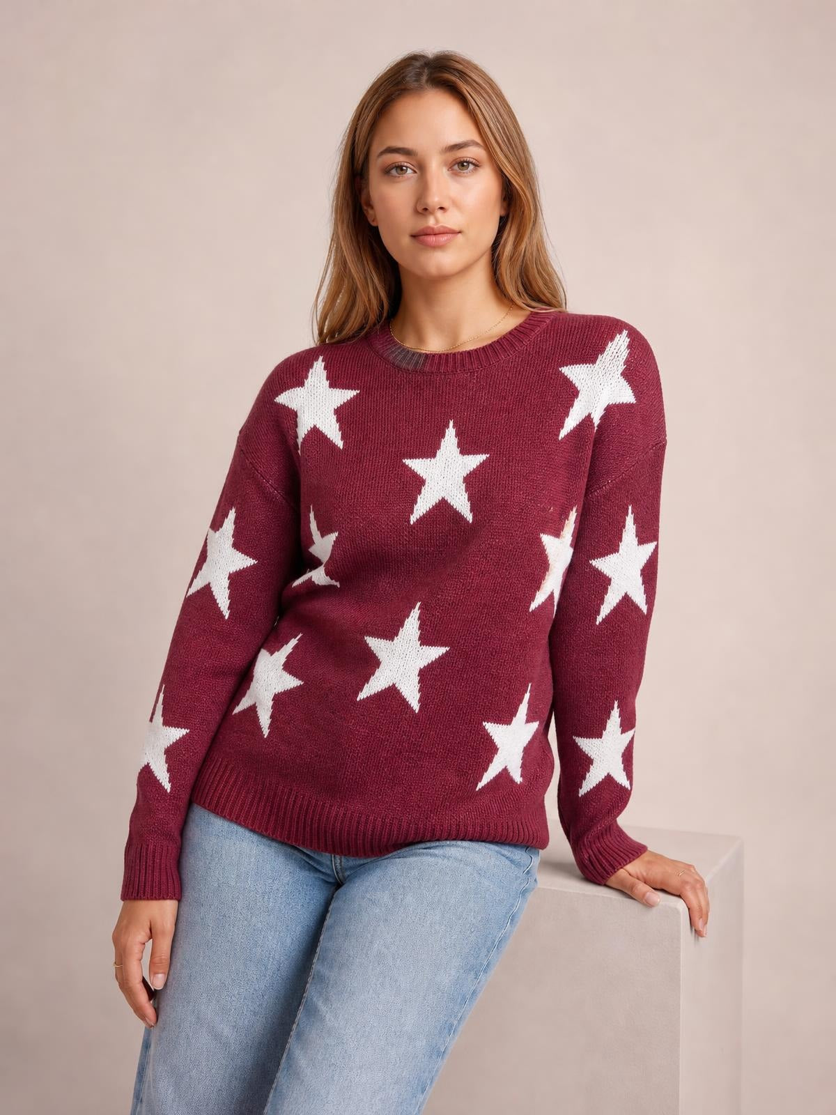 Model wearing a burgundy round-neck sweater with white star patterns, dropped shoulders, long sleeves, ribbed cuffs and hem, and a relaxed silhouette.