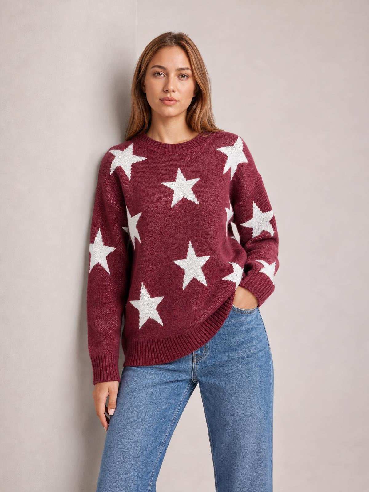 Model wearing a burgundy star-patterned round neck dropped shoulder sweater with a relaxed silhouette, ribbed cuffs and hem, and one hand in her jeans pocket.