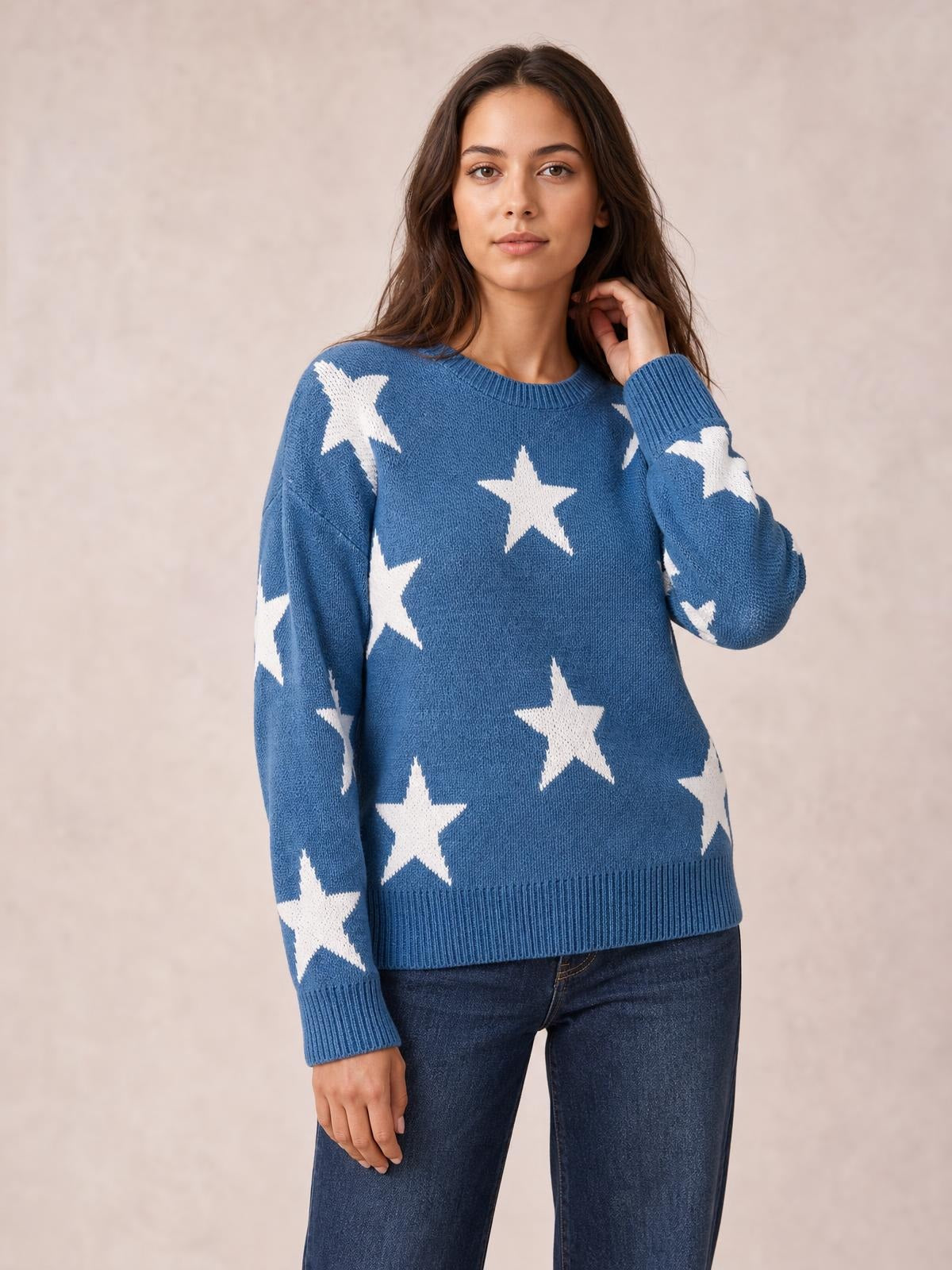 Model wears a blue star-print round neck dropped shoulder sweater with a relaxed silhouette, ribbed cuffs and hem, posing with one hand touching her hair.