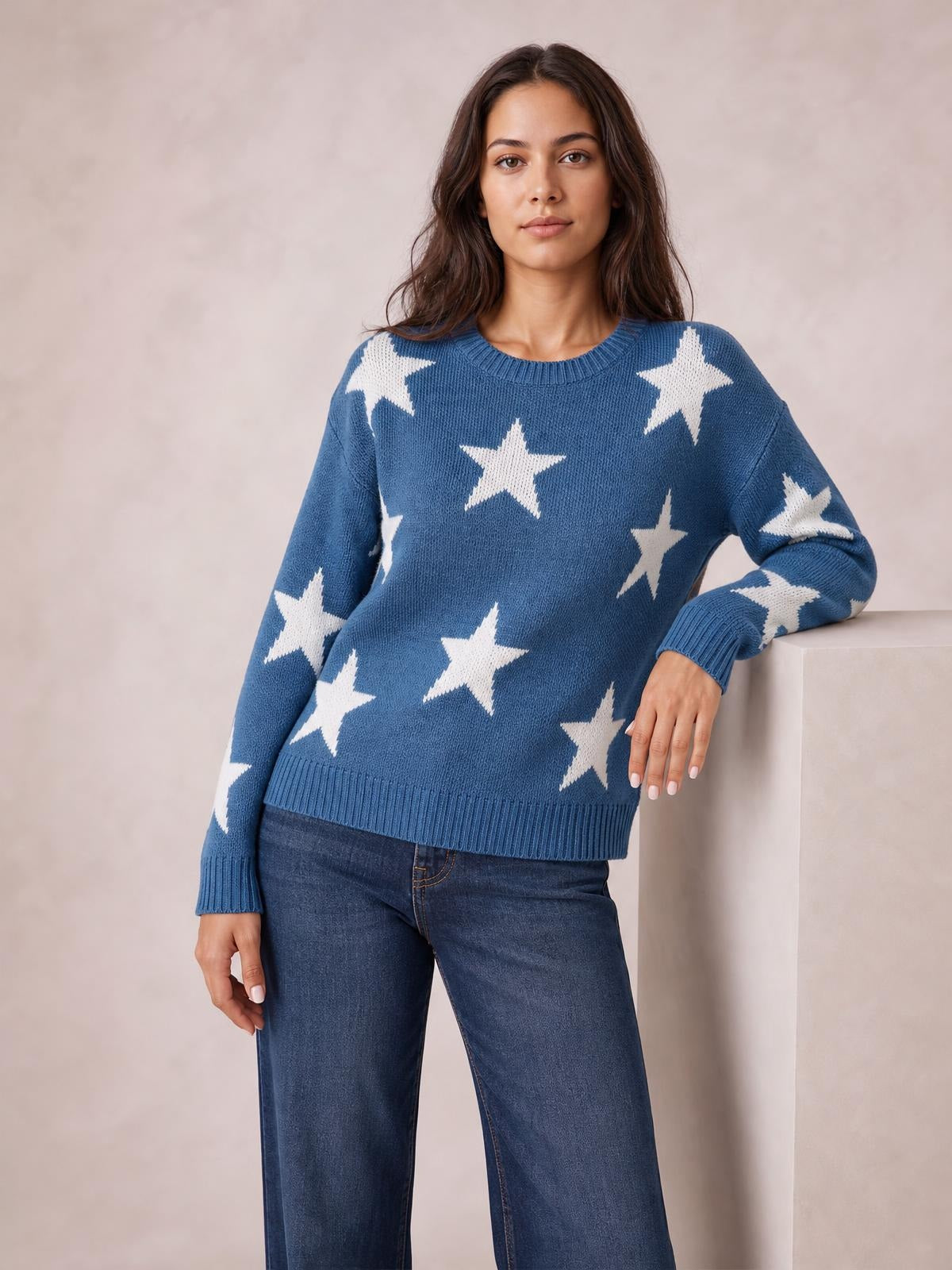 Model wears a blue round-neck dropped-shoulder sweater with white star patterns, ribbed cuffs and hem, and a relaxed silhouette.