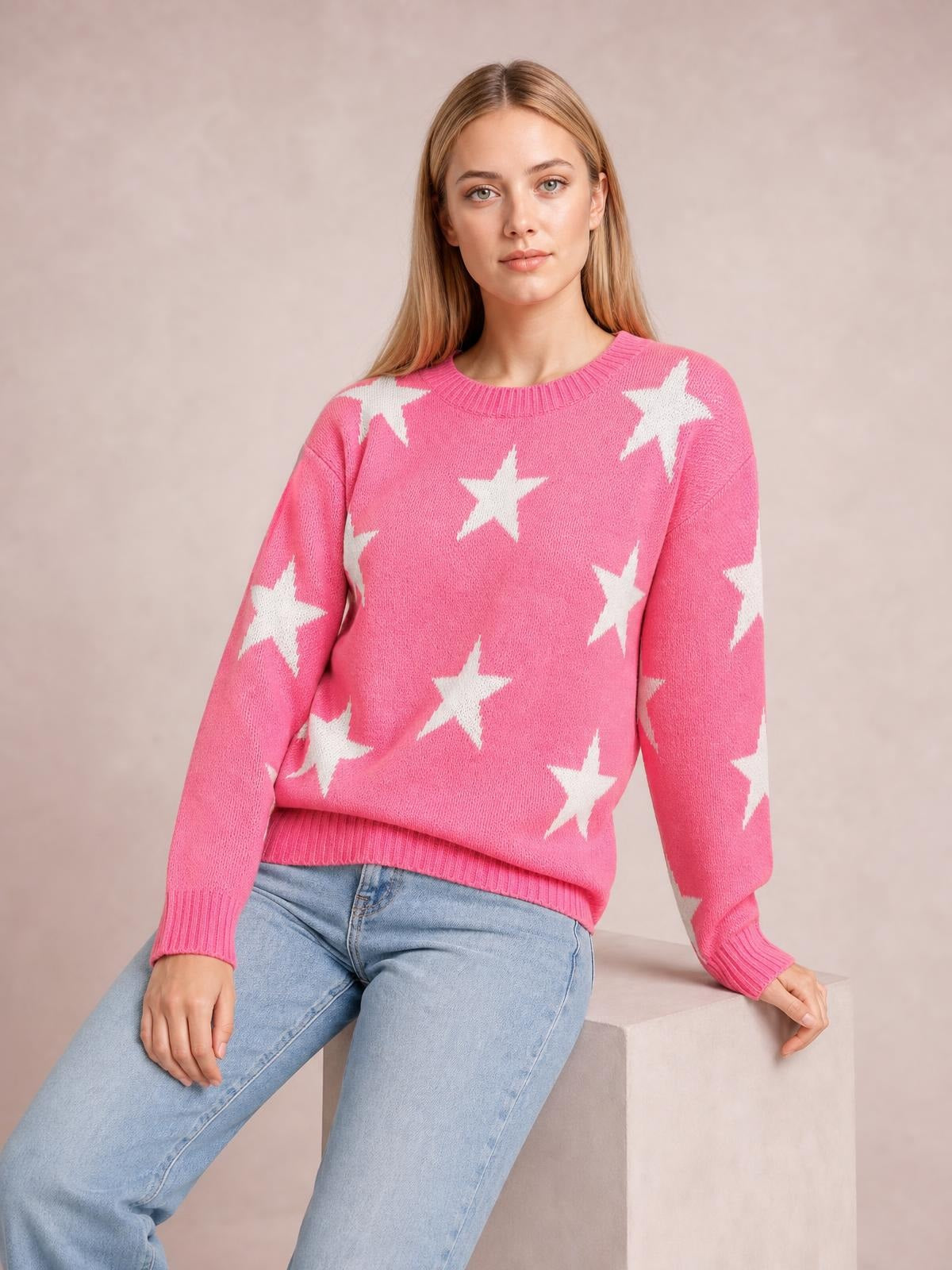 A model sits wearing a pink star-patterned round-neck sweater with dropped shoulders, a relaxed silhouette, ribbed cuffs, and a ribbed hem.