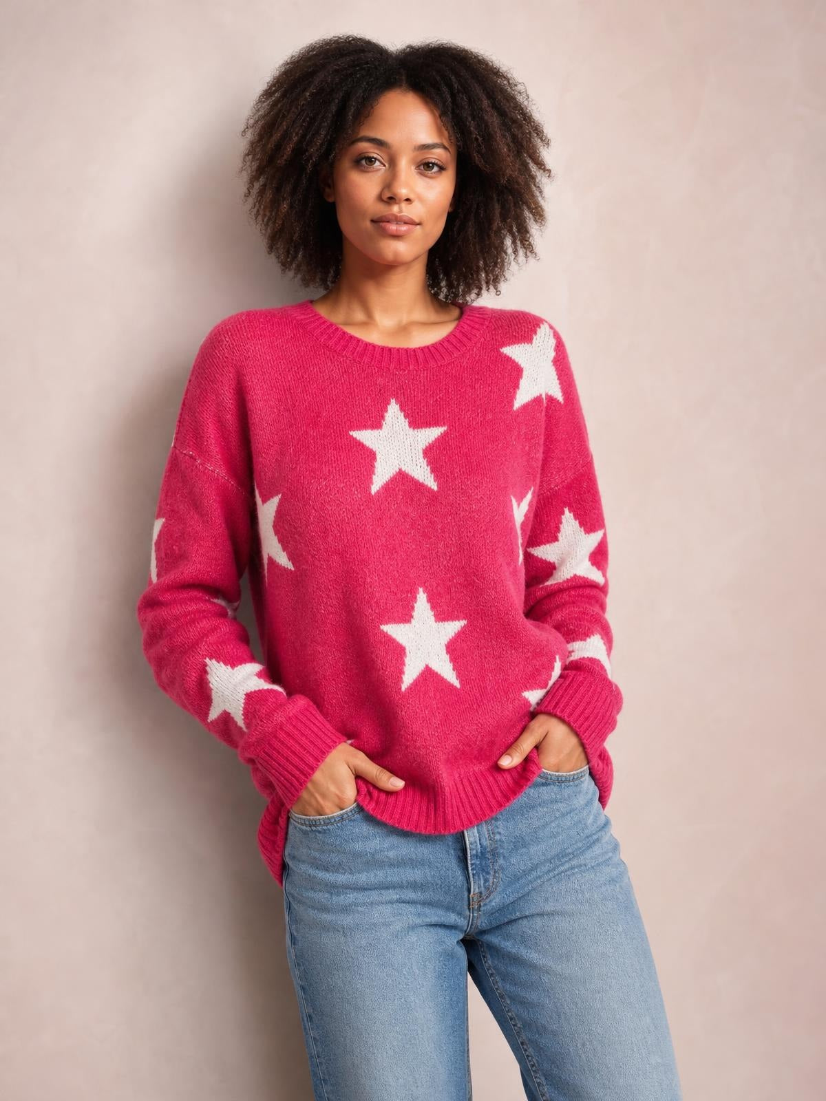 Model wearing a bright pink star-print round-neck sweater with dropped shoulders, ribbed cuffs and hem, standing with hands in her jeans pockets.