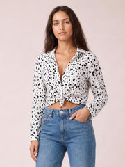 Model wearing a white animal print button-up shirt with a collared neckline, long sleeves, and a tied curved hem, posed with one hand in her jeans pocket.