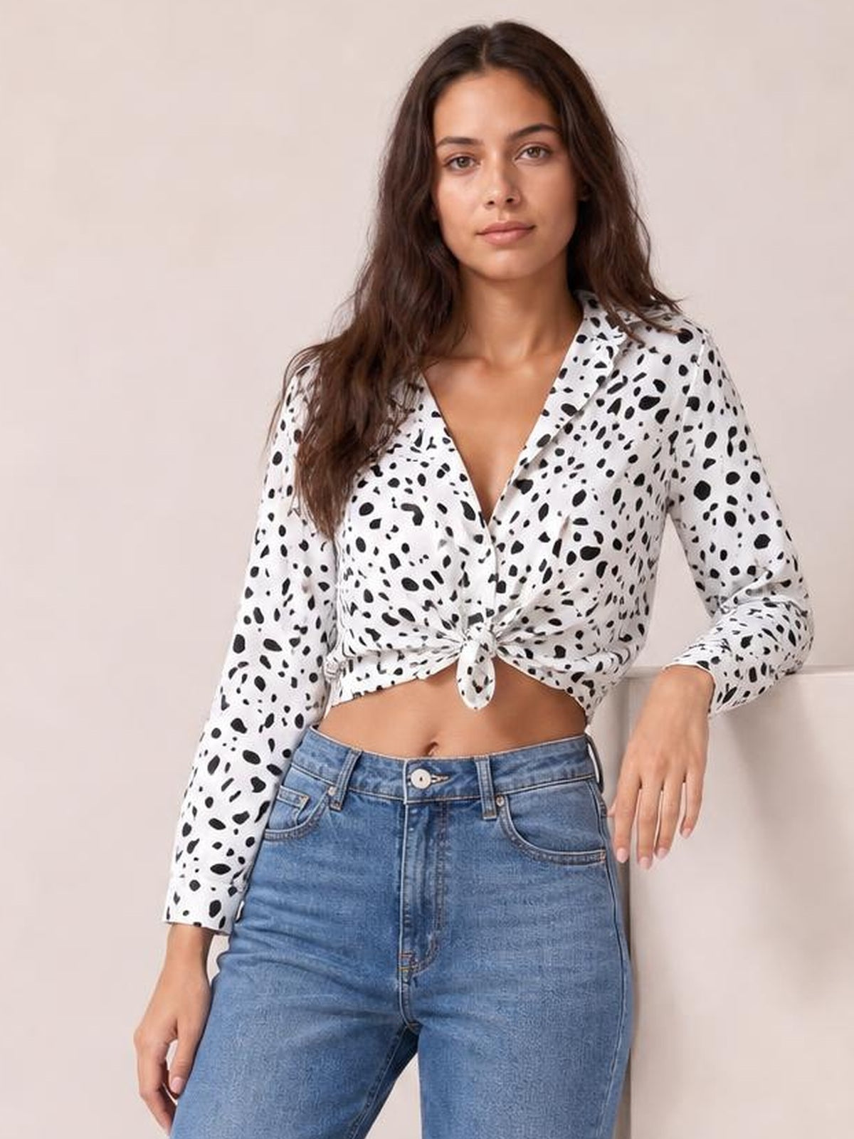 Model wearing a white and black animal print button-up shirt with a collared neckline, long sleeves, and a tied curved hem in a casual pose.