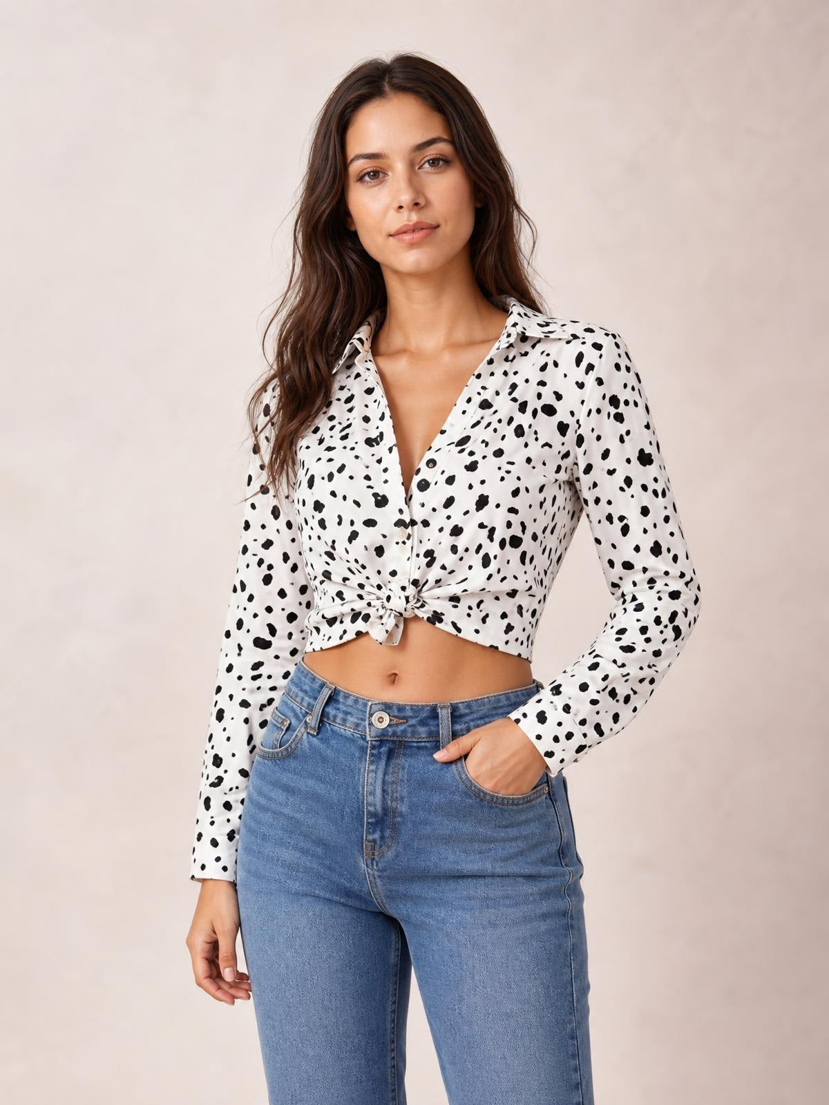 Model wearing a white and black animal print button-up shirt with a collared neckline, long sleeves, curved hem tied at the waist, and one hand in her jeans pocket.