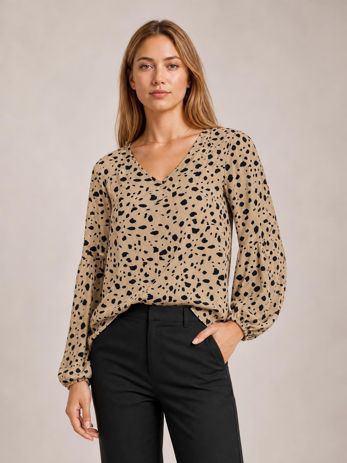 Model wearing a tan animal print V-neck blouse with long balloon sleeves, gathered cuffs, a relaxed silhouette, and a high-low hem.