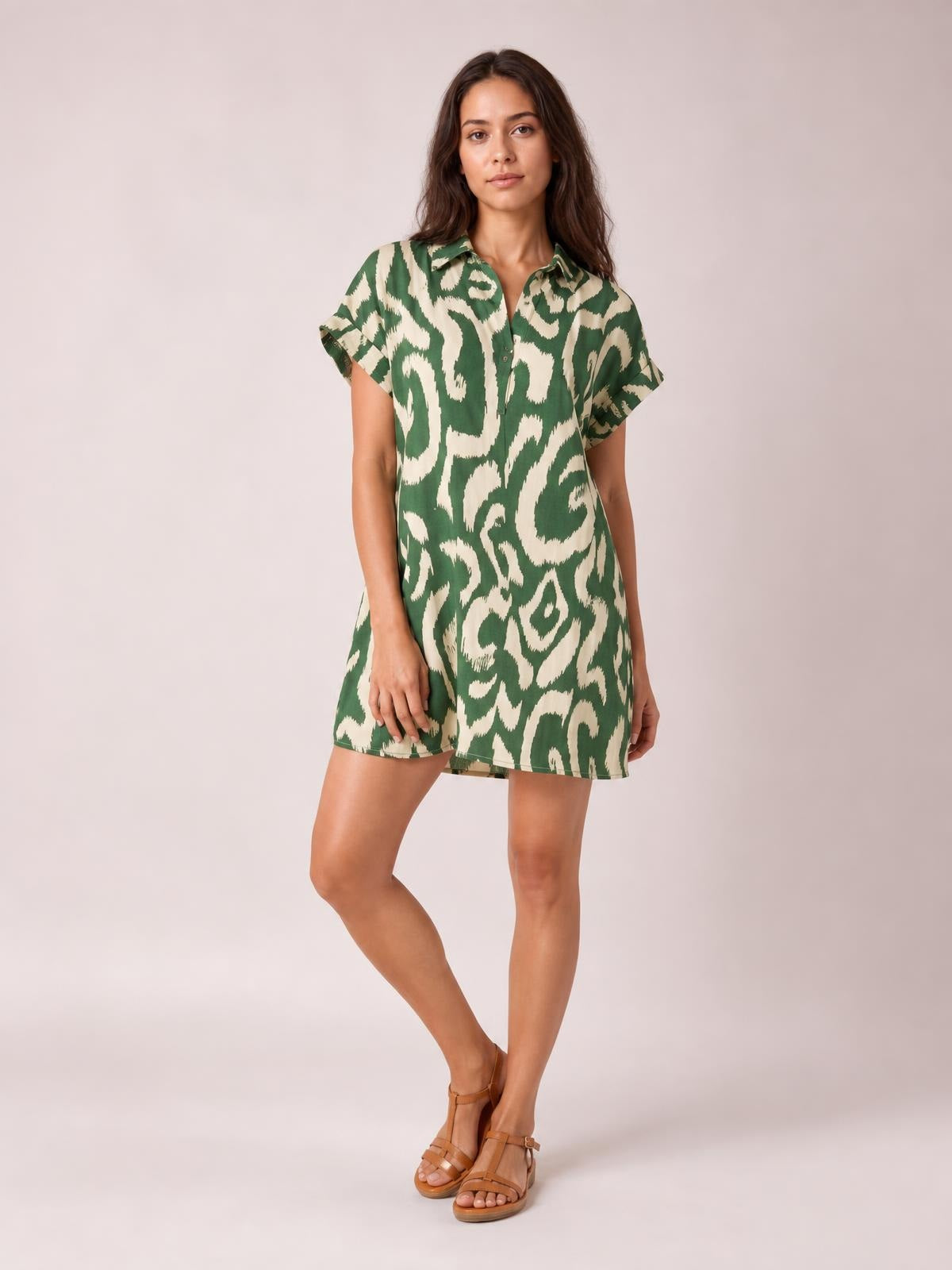 Model poses in a green and cream abstract printed shirt mini dress with a button-front collar, short sleeves, and a relaxed straight silhouette.