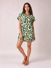 Model poses in a green and cream abstract printed shirt mini dress with a button-front collar, short sleeves, and a relaxed straight silhouette.