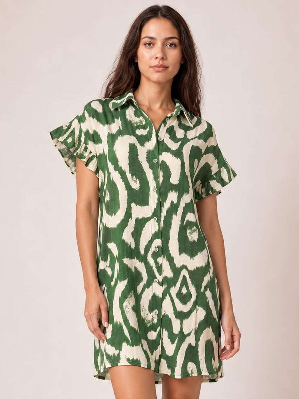 Model standing in a green and cream abstract printed mini dress with a collared shirt front, button closure, fluttering frill sleeves, and relaxed silhouette.