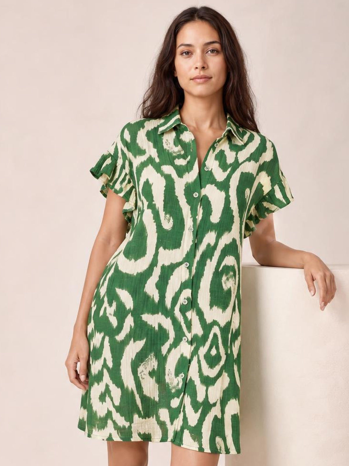 Model wearing a green and cream abstract printed mini shirt dress with a collared button front, layered frill sleeves, and a relaxed straight silhouette.