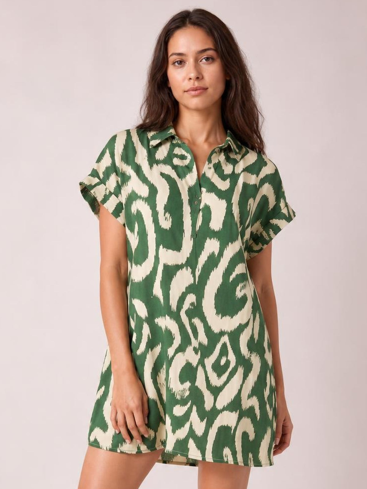 Model wears a green and cream abstract printed shirt-style mini dress with a collared button front, short cuffed sleeves, and a relaxed straight silhouette.