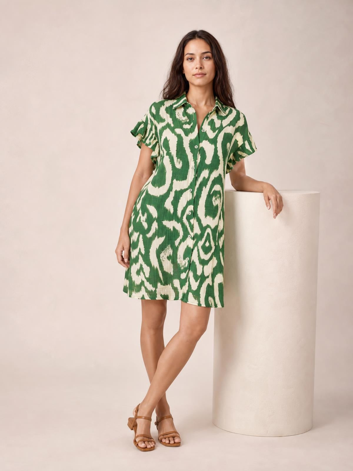 Model poses in a green abstract-print shirt mini dress with button-front construction, collared neckline, frill sleeves, and a relaxed straight silhouette.