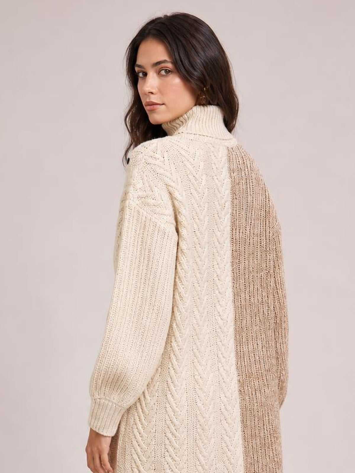 Model in a cream and taupe color block turtleneck sweater dress, shown from behind with long sleeves, ribbed knit panels, and a relaxed silhouette.