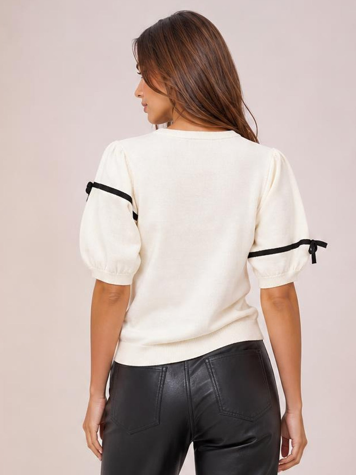 A model faces away wearing a white ribbed knit top with a round neckline, puff sleeves, black striped trim, and tied bow details.