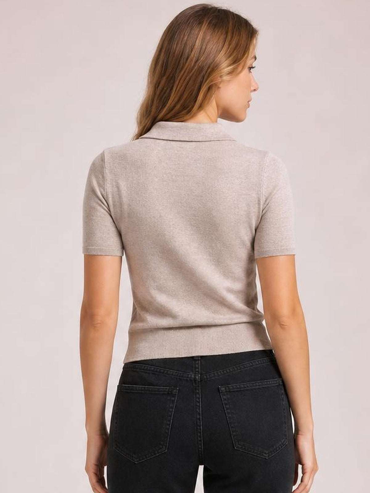 A model faces away wearing a light beige short sleeve sweater with a collared neckline, fitted silhouette, ribbed sleeve cuffs, and a ribbed hem.