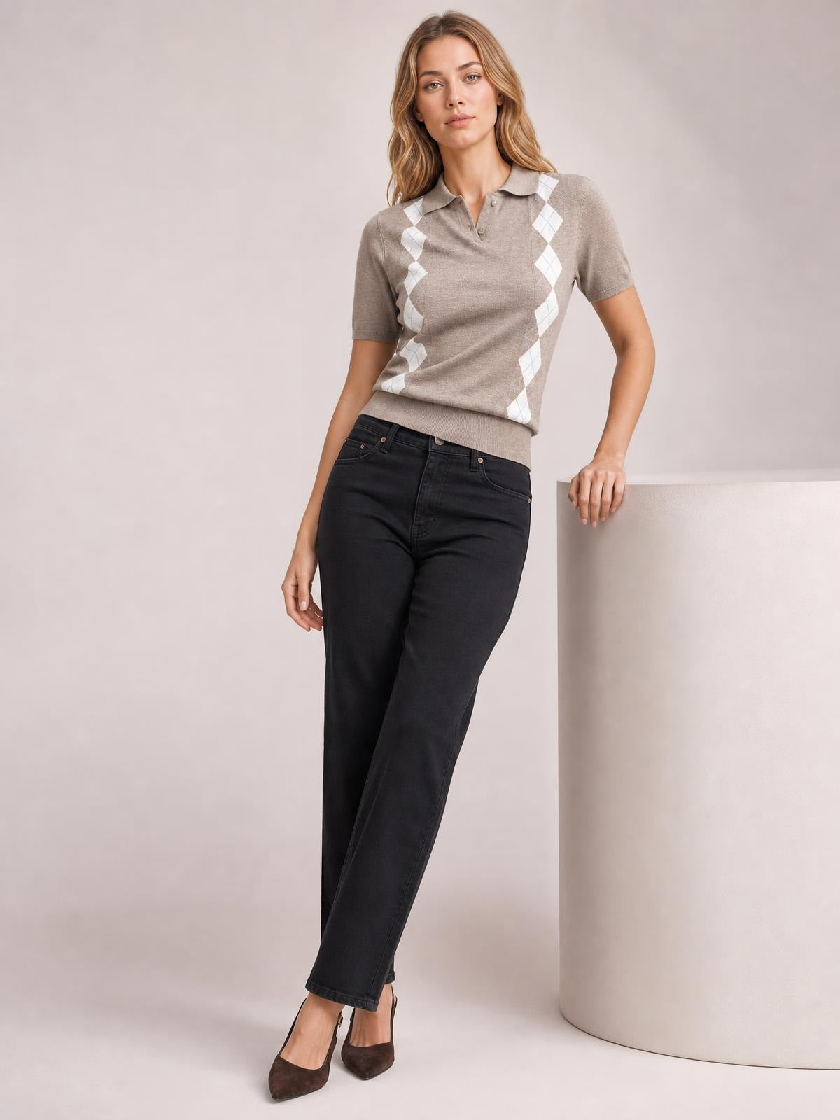 A model leans with one hand on a pedestal, wearing a taupe argyle patterned short sleeve sweater with a collared button placket and fitted silhouette.